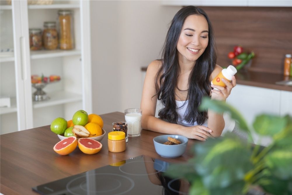Woman taking a daily multivitamin with breakfast Woman taking a daily multivitamin with breakfast